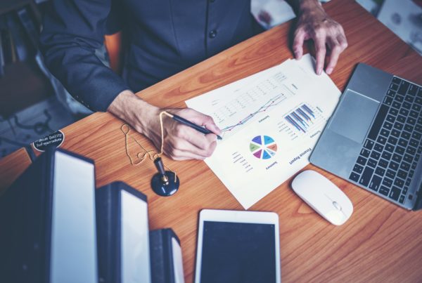 man noting down on piece of paper with graphs and charts