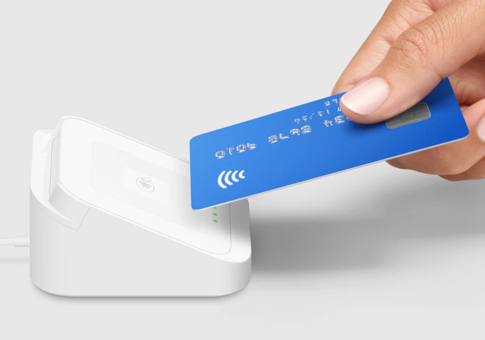 hand holding a credit card against a contactless payment device