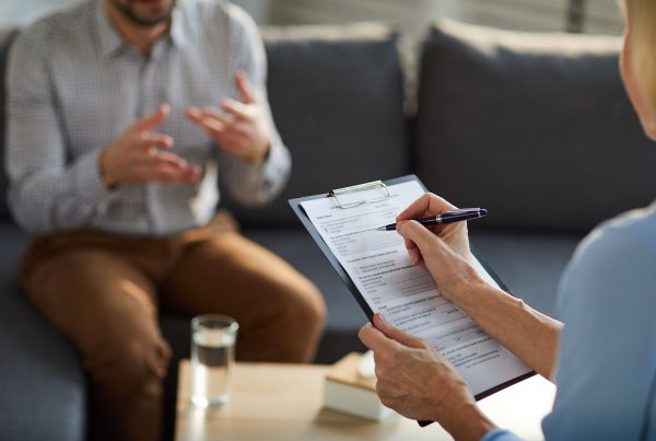 man explaining whilst a female listens and makes notes in therapy